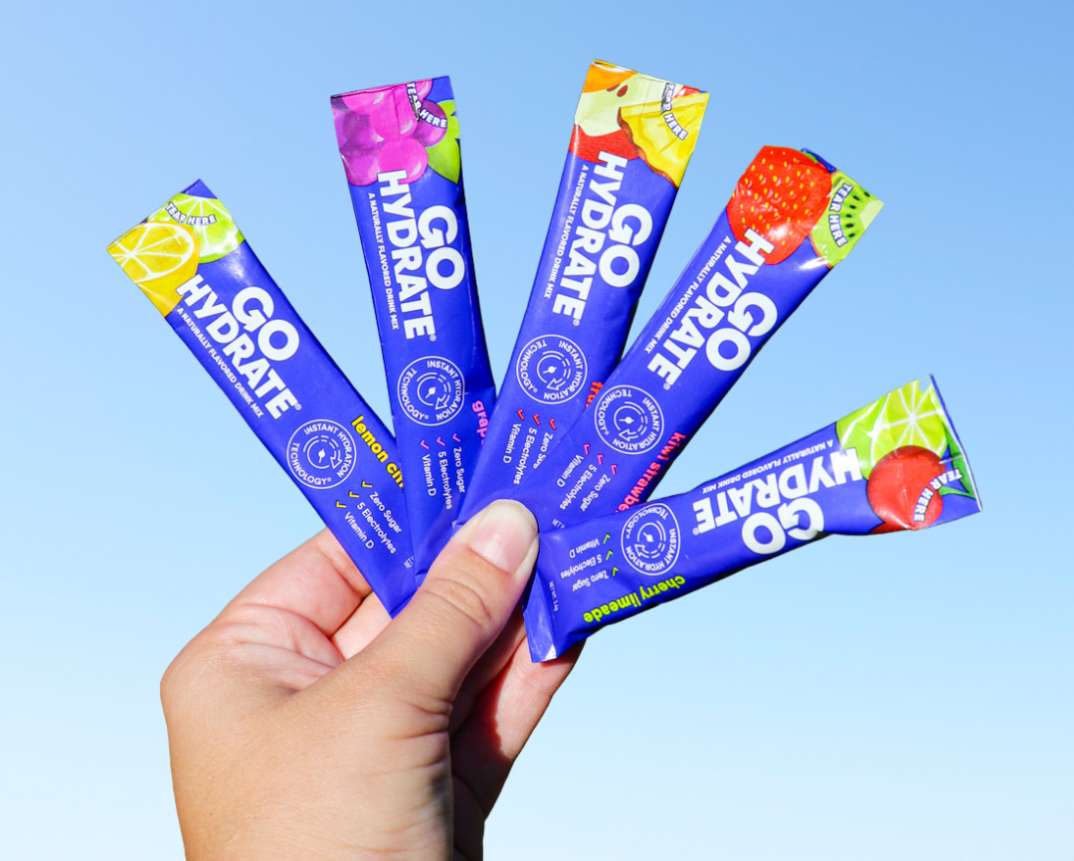 A hand holds 5 sachets of different flavors from the variety box