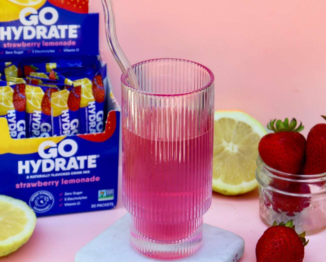 GoHydrate Strawberry Lemonade - Open Box with a clear glass with pink liquid a jar of strawberries and a lemon sliced open